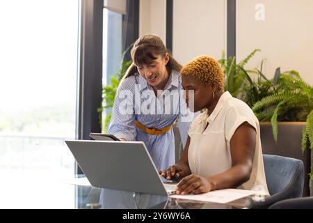 Collaborating on project, two women using laptop and tablet in modern office Stock Photo