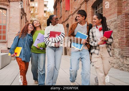 Group of diverse students walking together on campus, smiling and carrying notebooks, highlighting friendship, education, and student life in a university setting. Classmates enjoying school together. High quality photo Stock Photo