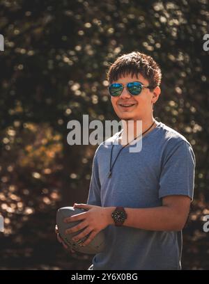 teen boy outside with football and sunglasses in fall Stock Photo