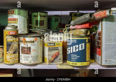 Old cans of latex, oil paint and varnish plus paint roller handles on a wooden shelf in a home workshop. Stock Photo