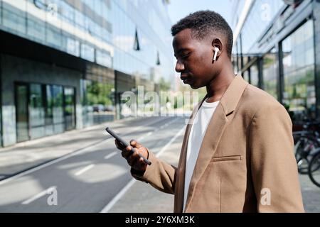 Young Black Manager Using Smartphone While Standing Outdoors Stock Photo