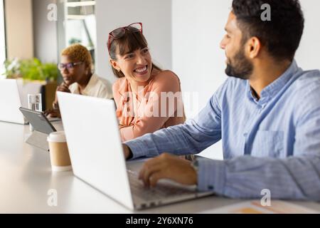 Working in office, colleagues discussing project using laptops and tablet, smiling Stock Photo