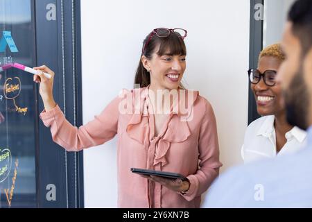 Leading meeting, woman with tablet writing on glass board, colleagues smiling Stock Photo