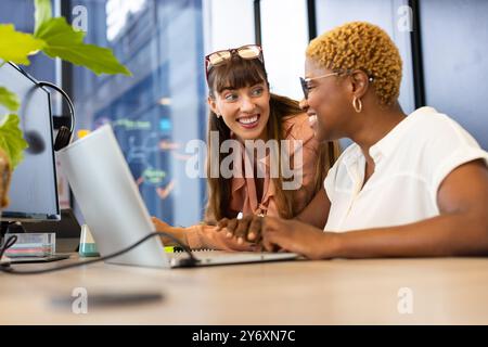 Collaborating at work, two women using laptop and discussing project in office Stock Photo