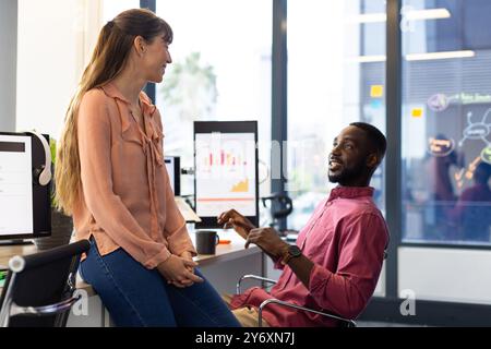 Discussing project progress, colleagues collaborating with charts on screens in modern office Stock Photo