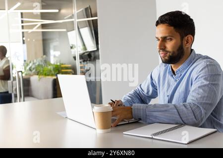 Working on laptop, man sitting at desk with coffee cup and notepad Stock Photo