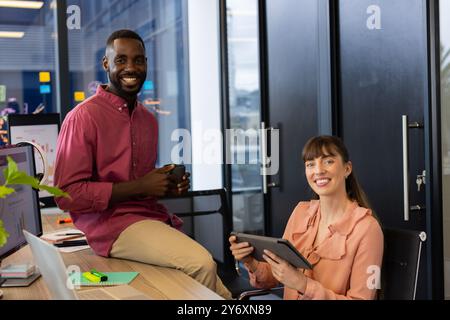 Collaborating on project, smiling colleagues in office using tablet and holding coffee Stock Photo