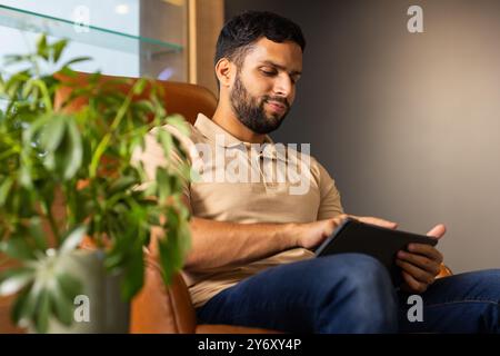 Using tablet, man sitting on chair and working in modern office setting Stock Photo