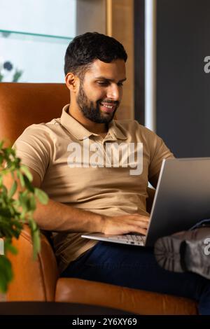 Smiling man using laptop while sitting on chair, working from home Stock Photo