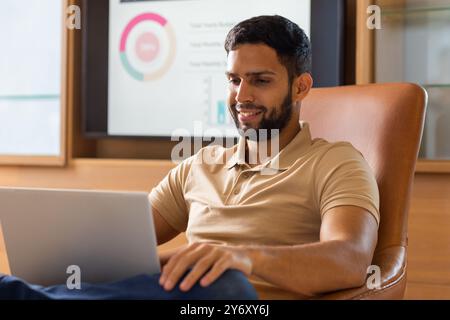 Using laptop, man smiling and working in office with data charts in background Stock Photo