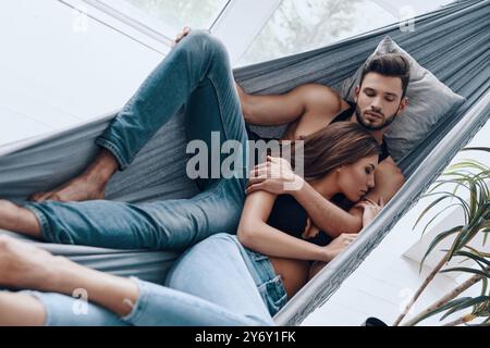 Loving couple. Top view of beautiful young couple embracing while sleeping in the hammock indoors Stock Photo
