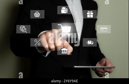 A businessman in a suit using a tablet with various e-commerce icons floating in the air, symbolizing online shopping and digital transactions. Stock Photo