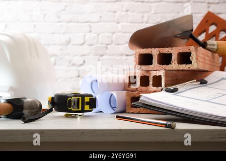 Architect's desk with plans and construction materials on white wooden table in office. Front view. Stock Photo