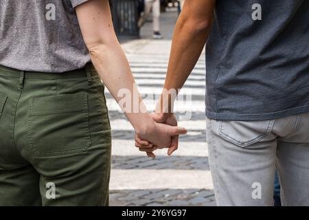 Close-up of diverse couple holding hands while crossing street. Interracial relationship, unity and love concept. Urban setting with pedestrian crossi Stock Photo