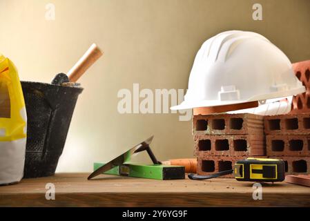 Construction materials such as bricks, cement and tools on a wooden board and brown isolated background. Front view. Stock Photo