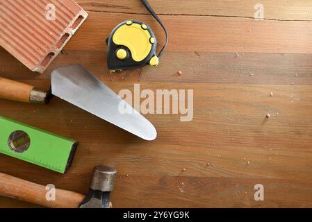 Construction tools such as trowel, level, tape measure, hammer and brick on wooden plank. Top view. Stock Photo