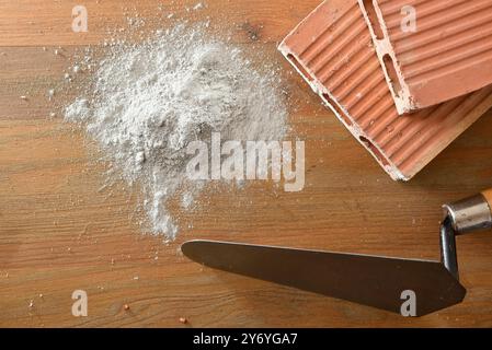 Background with tools and construction materials with construction trowel, bricks and cement powder on wooden board. Top view. Stock Photo