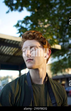 Young man with curly red hair gazing thoughtfully outdoors Stock Photo