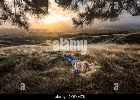 Teen lying in grass on hilltop in golden light Stock Photo