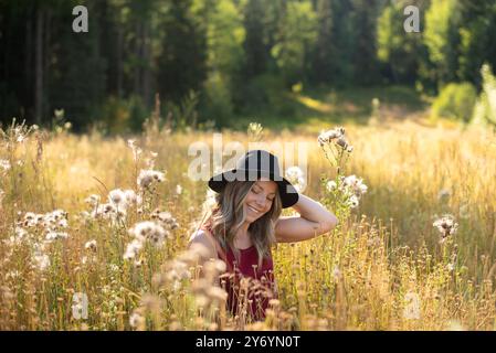 Woman sitting in grassy autumn meadow smiling in the sunshine Stock Photo