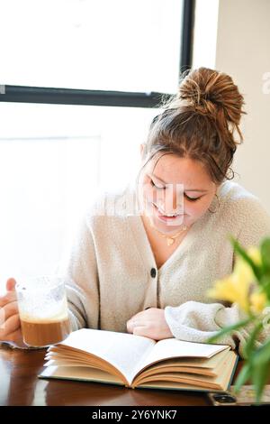 Young lady smiling while reading a book and holding a cup of cof Stock Photo