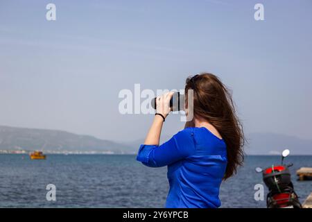 Young woman with long hair is looking through binoculars at the sea Stock Photo