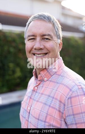 Smiling senior man in plaid shirt enjoying outdoor time with diverse friends, at home Stock Photo