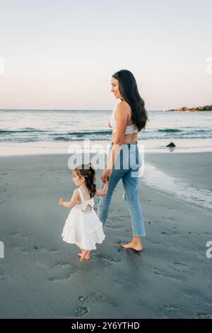 Mother and daughter holding hands, walking barefoot along the beach Stock Photo