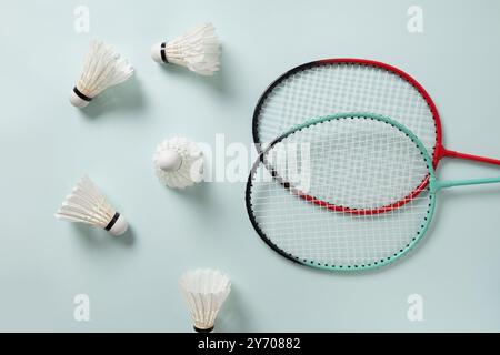 White feather badminton shuttlecocks and two badminton rackets on light blue background. View from above. Concept racket sport. Leisure games. Stock Photo