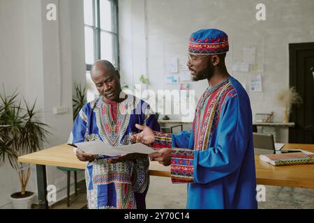 African American coworkers in traditional clothes discussing new startup while working offline in modern office Stock Photo