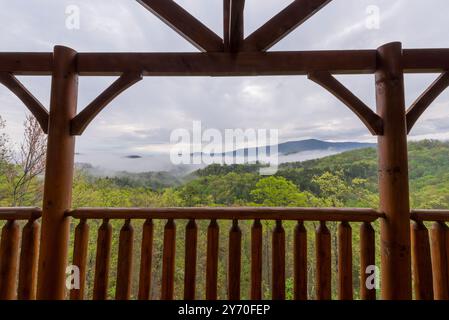 A stunning view of the mist-covered Smoky Mountains as seen from a rustic cabin balcony, framed by timber beams. Perfect depiction of nature and tranq Stock Photo