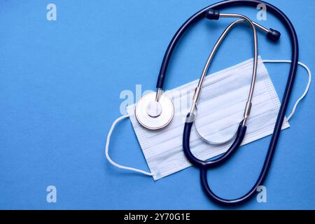 On the table lay a stethoscope and a protective respirator mask on a blue background. Medical banner template with copy space, header layout. Stock Photo