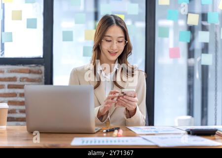 Happy young business woman working on her project at the office and checking her messages on her phone Stock Photo
