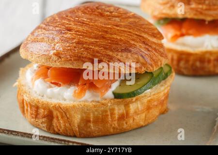 Delicious brioche sandwich with smoked salmon, cream cheese, cucumber and olives close-up on plate on table. Horizontal Stock Photo