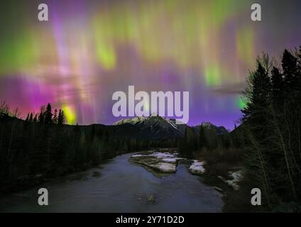 Vibrant aurora borealis lighting up the sky above a frozen river and snow covered mountains Stock Photo
