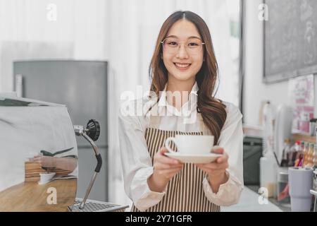 Happy young female barista holding a cup of coffee to serve her customer Stock Photo