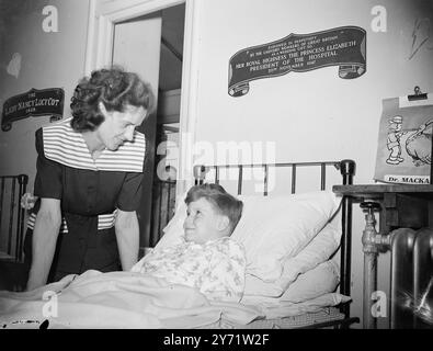 Laundry 'Queen' visits Queen Elizabeth Hospital.   Britain's laundry workers were represented at the Dedication of the Cot ceremony at the Queen Elizabeth Hospital for Children, Hackney, this afternoon, when Margaret Sterne of Old Hall Laundry, Leeds, the first national Lorna, paid a visit to the hospital. Last December, Margaret visited the same hospital, armed with a huge laundry basketful of toys for the kiddies, a gift from North Eastern laundry workers.     Picture shows :- 'His welcome visitor' - Thomas Guy, 7 years old, has a smile for Margaret Sterne, the Laundry 'Queen', when she visi Stock Photo