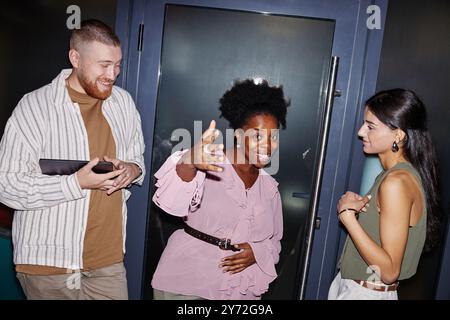 Medium shot of diverse creative team of three smiling office workers in smart casual clothing playfully posing for camera while having fun at workplace in business center, camera flash, copy space Stock Photo