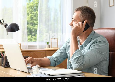 Mature male freelancer talking by mobile phone at table in office Stock Photo
