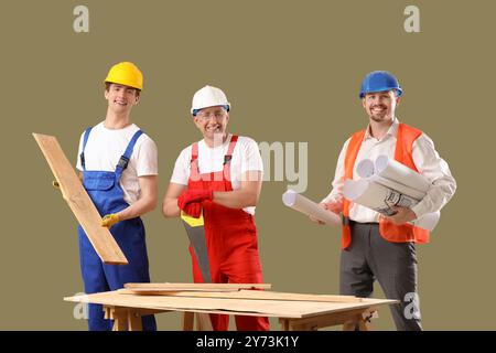 Team of male builders with wooden planks and house plans on green background Stock Photo