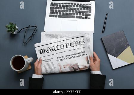 Woman reading newspaper at workplace with coffee and laptop on grey background Stock Photo