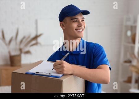 Young courier with parcel and clipboard in room Stock Photo
