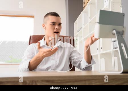 Confused young man with earphones and tablet computer video chatting in office Stock Photo