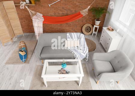 Interior of stylish living room with grey sofa, surfing board and hammock Stock Photo