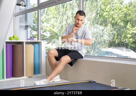 Sporty young man checking pulse near window in gym Stock Photo