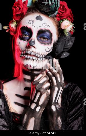 Headshot portrait of woman with flower at Day of the Dead event to remember the deceased, celebrating their memory. Lady holding black rose for Mexican holiday of remembrance for those who have passed Stock Photo