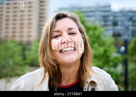 Portrait of cheerful older blonde woman posing outdoors with unfocused background urban garden. Stock Photo