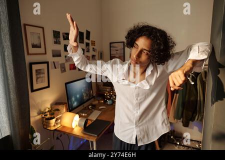Young man with hangover looking at daylight through fingers while standing in messy domestic room after booze Stock Photo
