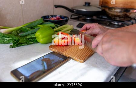 A technology use concept with a person preparing a meal in the kitchen by following an online recipe on a smartphone. Stock Photo