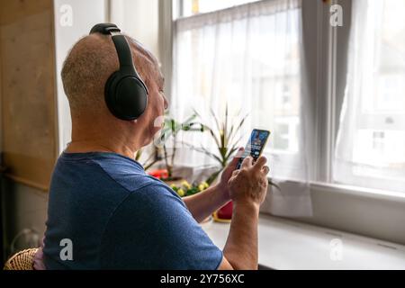 A senior man relaxing at home listening to online music with wireless headphone and a smartphone. A technology use concept. Stock Photo